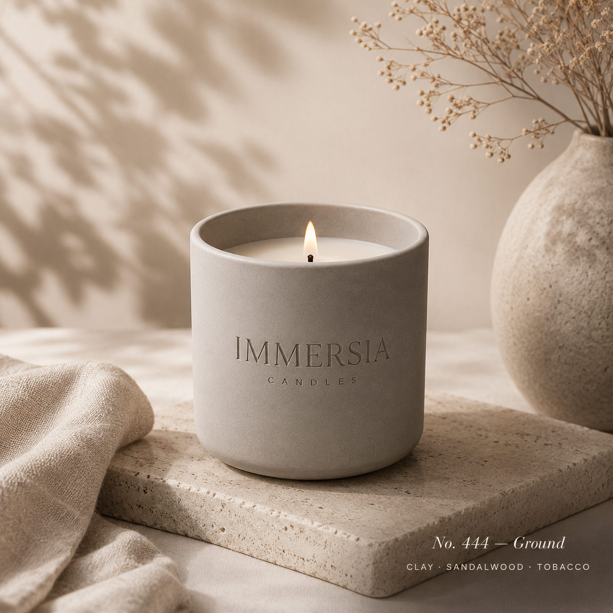 A warm ivory ritual candle resting on travertine with eucalyptus and pampas grass